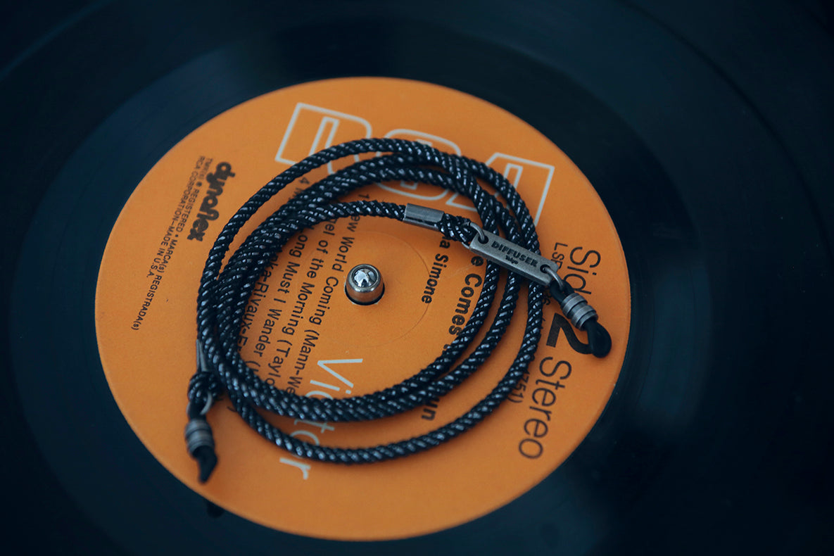 A close-up of a black braided headphone cable with silver metal connectors, laid over an orange vinyl record label on a black vinyl record.