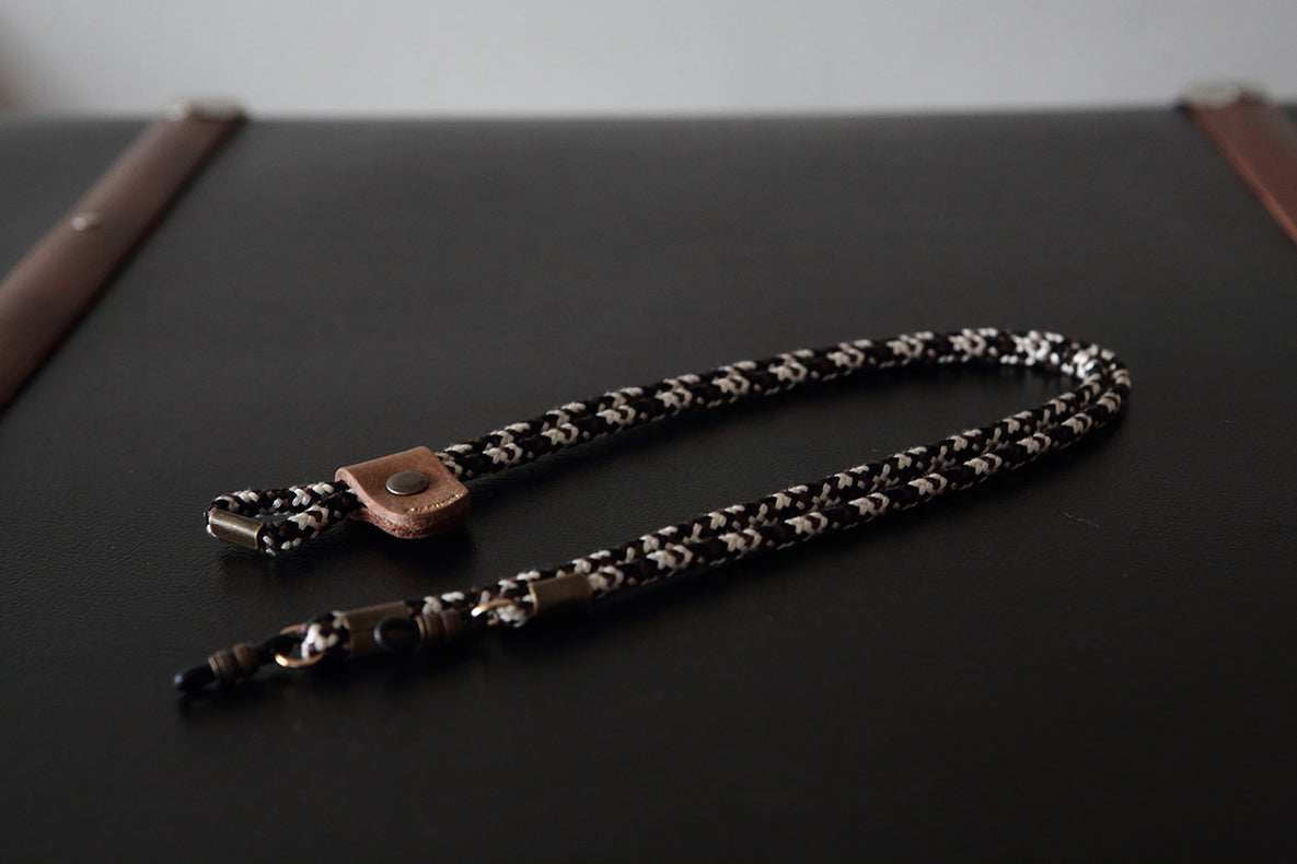 A black and white patterned braided strap with a copper-toned snap button and silver metal hardware, resting on a dark surface.