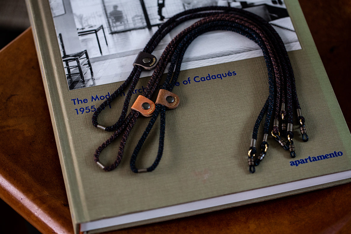 A close-up of braided black and brown leather lanyards with tan leather loops and metal snap closures, laid on top of a book.