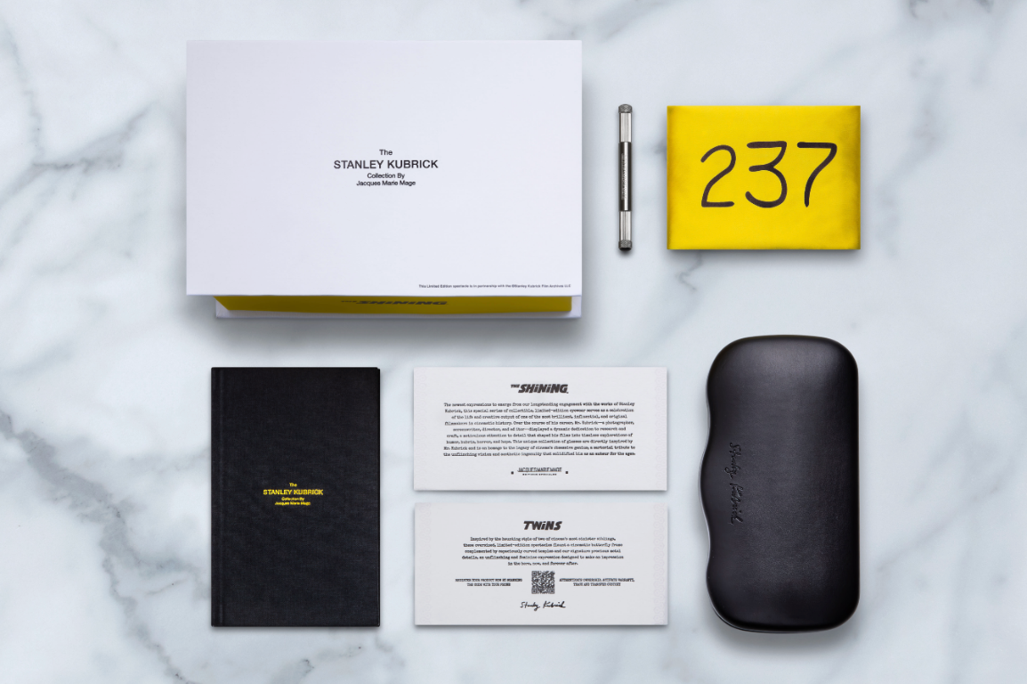 A Stanley Kubrick by JMM: Twins set from Jacques Marie Mage is displayed on marble, featuring a white box, yellow card with 237, black notebook, various cards, and limited-edition spectacles in a black case.