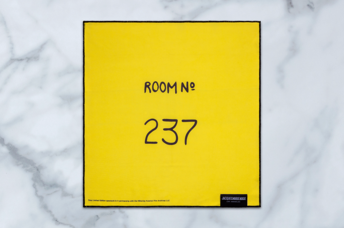 A yellow square cloth by Jacques Marie Mage, made for Stanley Kubrick by JMM: Twins eyewear, features ROOM № 237 in black at the center and a small label in the bottom right corner, shown on a white marble surface.