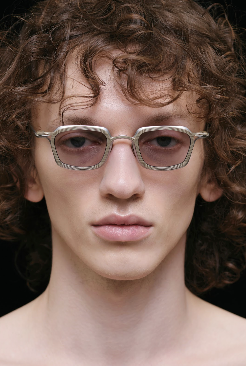 Model wearing silver RIGARDS rectangular glasses with lightly tinted lenses and layered metal rims, photographed in a close-up portrait.