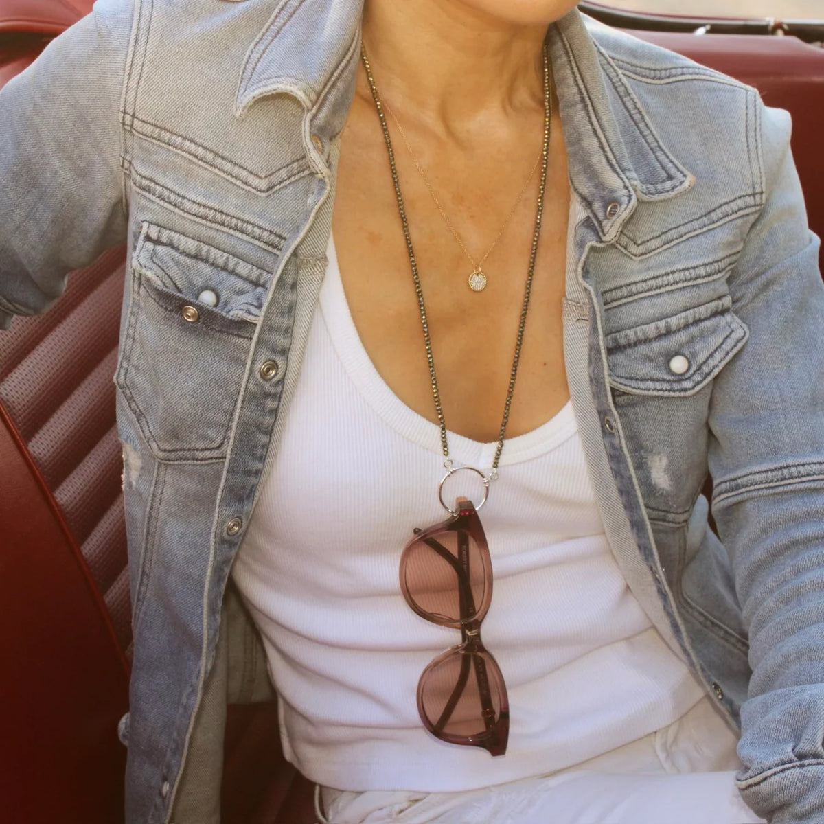 La Loop Stella black spinel beaded necklace featuring a central gold-plated circular metal loop holding a pair of brown sunglasses.
