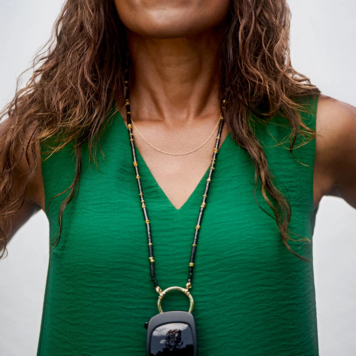 Person wearing a green sleeveless top with a necklace featuring a small bag pendant.