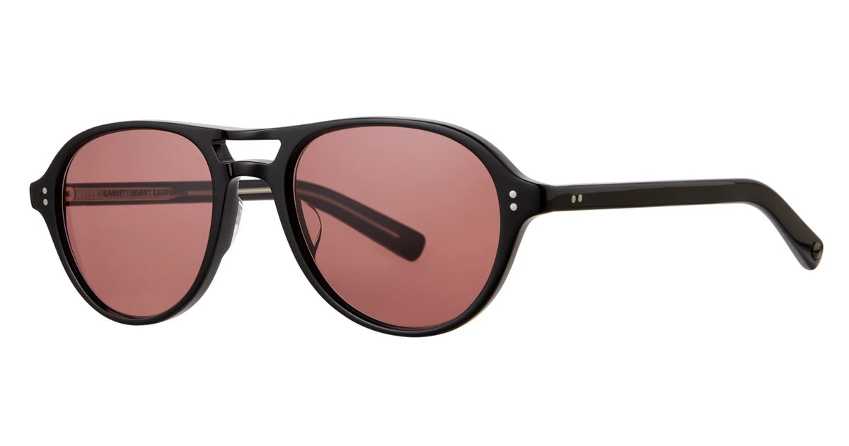The Garrett Leight Hancock by Garrett Leight are black round sunglasses featuring two small silver dots on the front corners and pink tinted lenses, displayed against a white background. These stylish frames provide reliable UV protection, combining practicality with fashion-forward design.