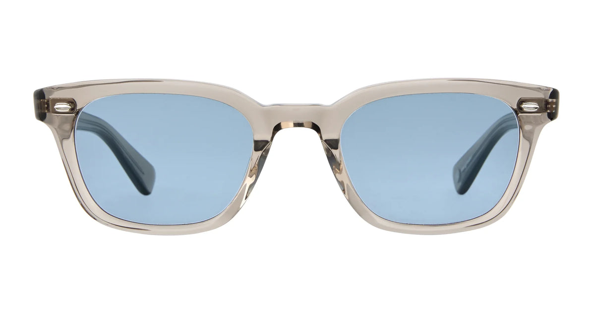The Garrett Leight Lugo sunglasses by Garrett Leight feature a beige translucent rectangular wayfarer design with thick frames and blue-tinted lenses that provide UV protection, displayed from the front against a white background.