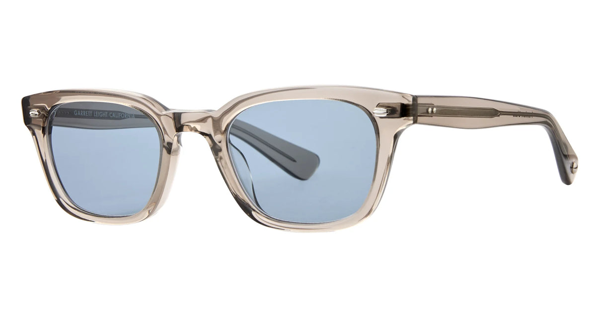 The Garrett Leight Lugo eyeglasses by Garrett Leight feature translucent beige square frames with blue-tinted, UV-protective lenses, displayed at an angle on a white background.
