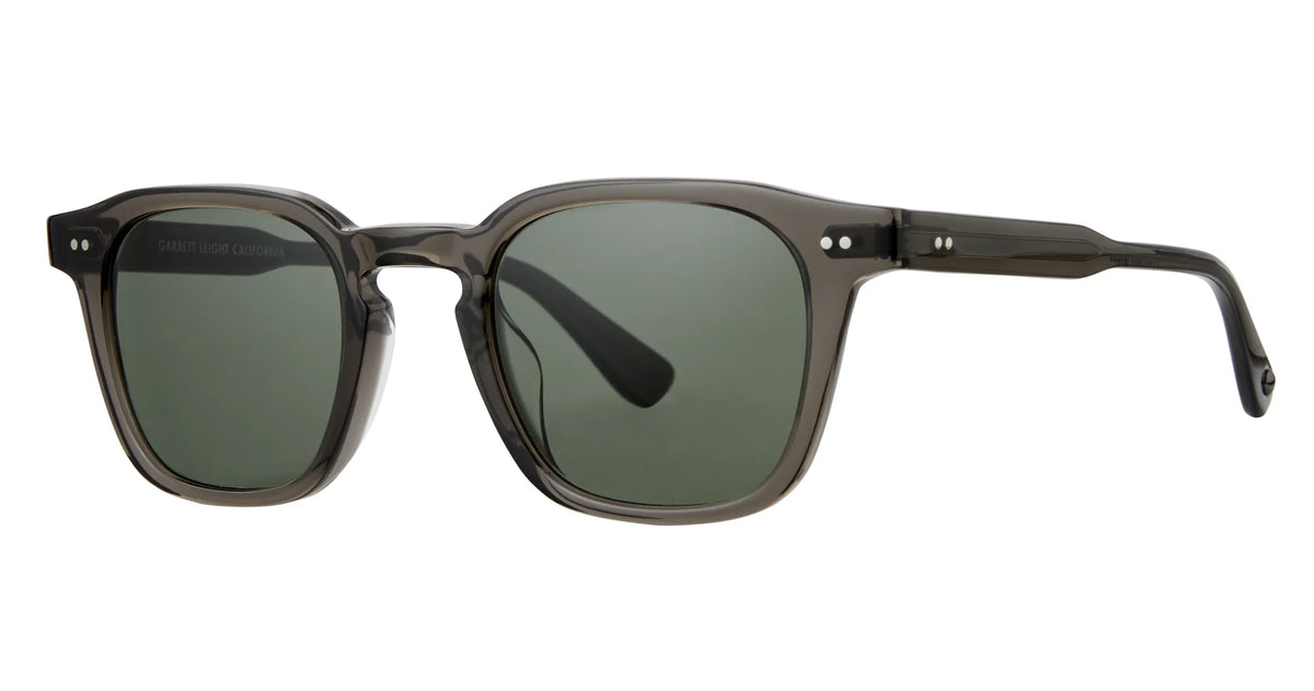 The Garrett Leight Verdugo sunglasses feature a rectangular shape with a translucent dark gray frame, dark green premium glass lenses, and a keyhole bridge. Each side of the front frame is adorned with two small silver accents. Designed by Garrett Leight, these sunglasses provide 100% UV protection for both style and safety.