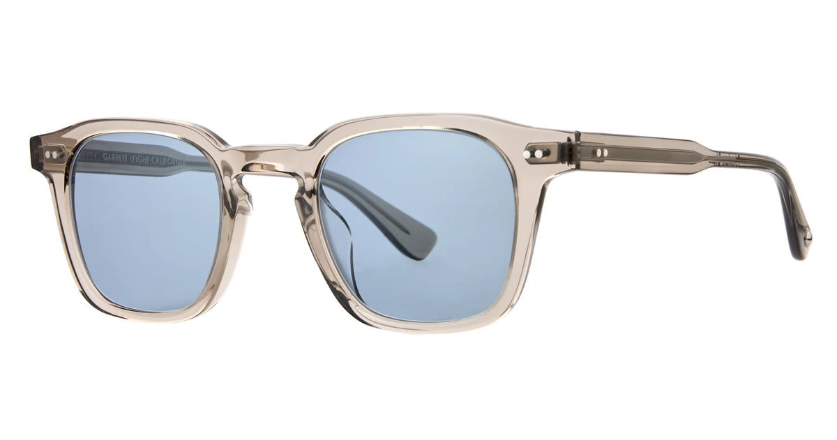 Translucent beige square sunglasses with thick frames and light blue premium glass lenses that provide 100% UV protection—the Garrett Leight Verdugo by Garrett Leight is pictured on a white background.