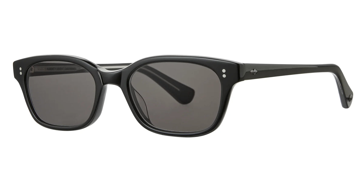 The Garrett Leight Chaparral by Garrett Leight features black rectangular sunglasses with thick frames, small silver accents near the hinges, and dark tinted lenses that provide 100% UV protection, showcased against a white background.