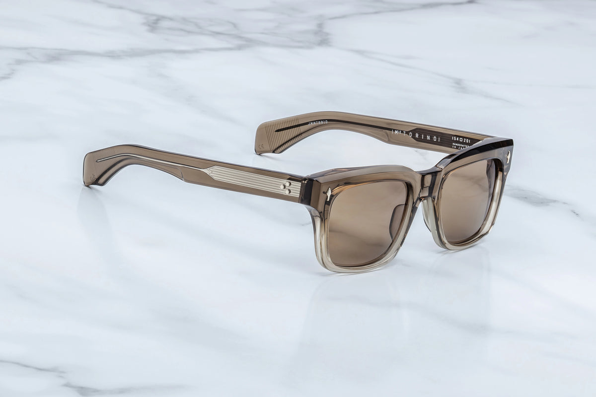 Jacques Marie Mage Torino sunglasses with a translucent brown rectangular, ’60s-inspired frame and light brown lenses, resting on a white marble surface.