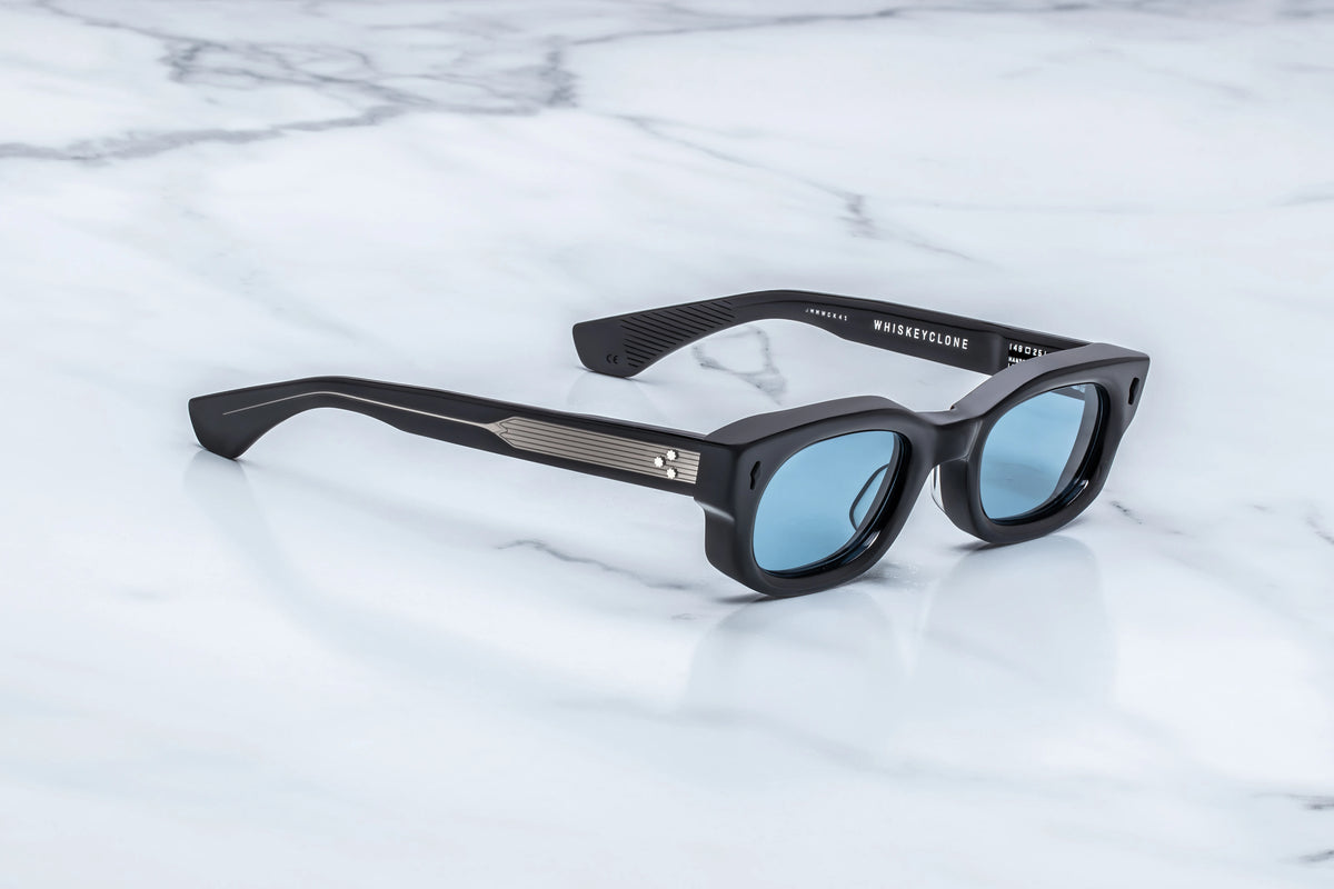 Jacques Marie Mage Whiskeyclone 90s-style rectangular black sunglasses with light blue reflective lenses and silver-toned metal detailing on the temples.