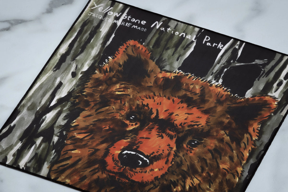 Square fabric print of Jacques Marie Mage Yellowstone VII: Junction Butte In Lodgepole, featuring a painted brown bear against a forest backdrop with the text Yellowstone National Park at the top.