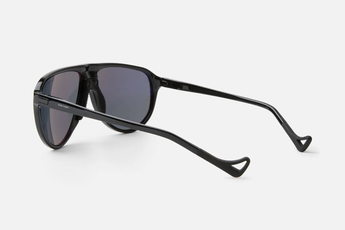 The District Vision Yukari Windshield by District Vision is shown from the back and side, featuring black frames with dark lenses in a sleek, modern design. Curved earpieces evoke the classic aviator silhouette, while the six base frame provides both comfort and style—all presented against a plain white background.