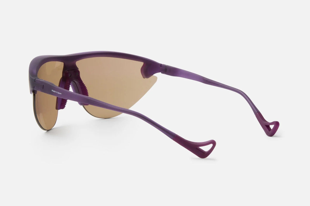 District Vision Yukinori Range Finder by District Vision in purple, shown from a rear side angle. These wraparound cycling eyewear feature brown-tinted lenses and thin, curved arms ending in distinctive open-loop tips. Set against a plain white background.