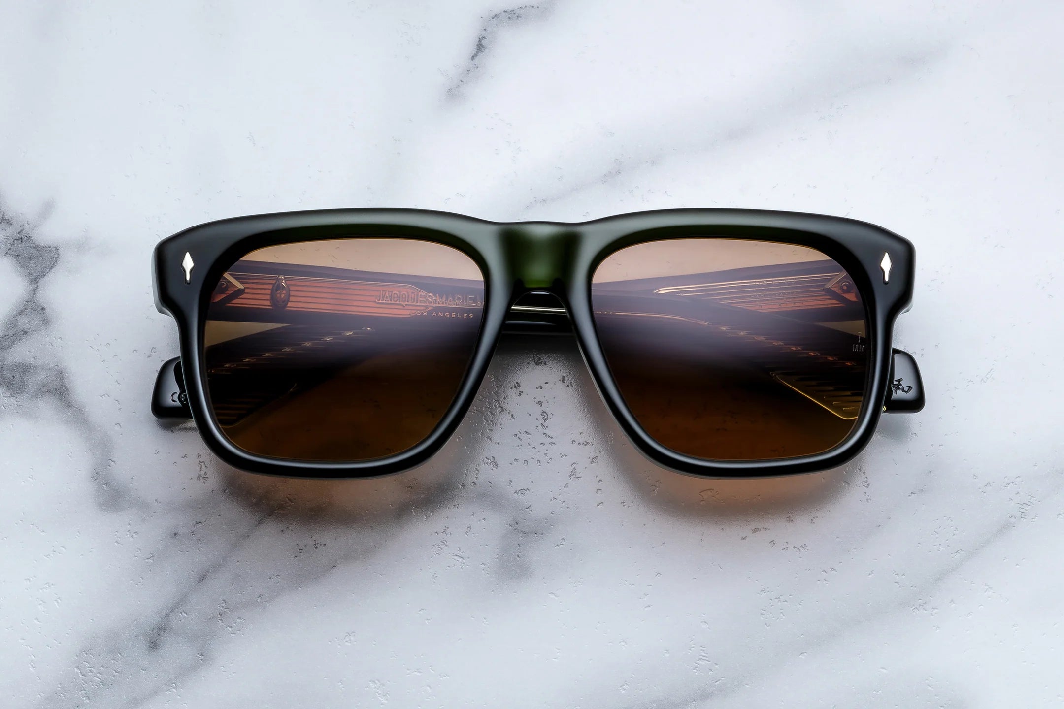 A pair of square-frame sunglasses with a glossy black frame and brown gradient lenses, resting on a white marble surface.
