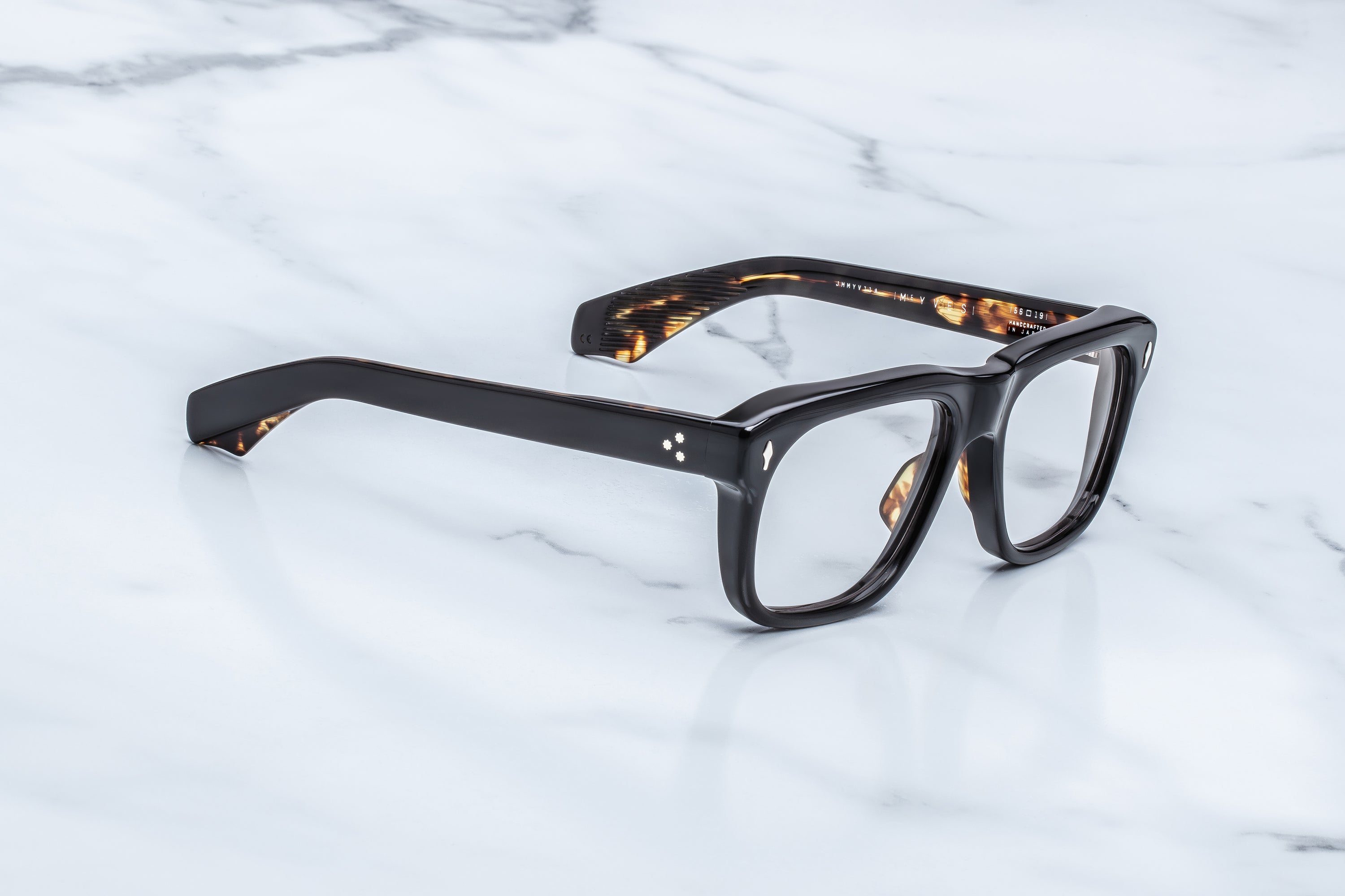 Jacques Marie Mage Yves by Jacques Marie Mage—thick, black rectangular eyeglasses featuring subtle tortoiseshell detailing on the inner arms, inspired by iconic frames favored by Yves Saint Laurent—displayed on a white marble surface.