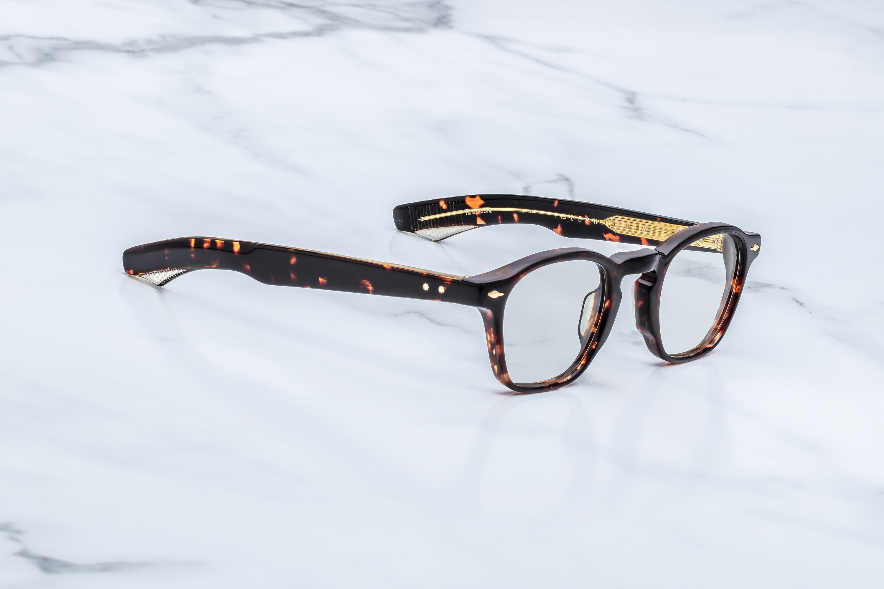 A pair of round-frame eyeglasses with a dark brown and amber tortoiseshell acetate frame, resting on a white marble surface.