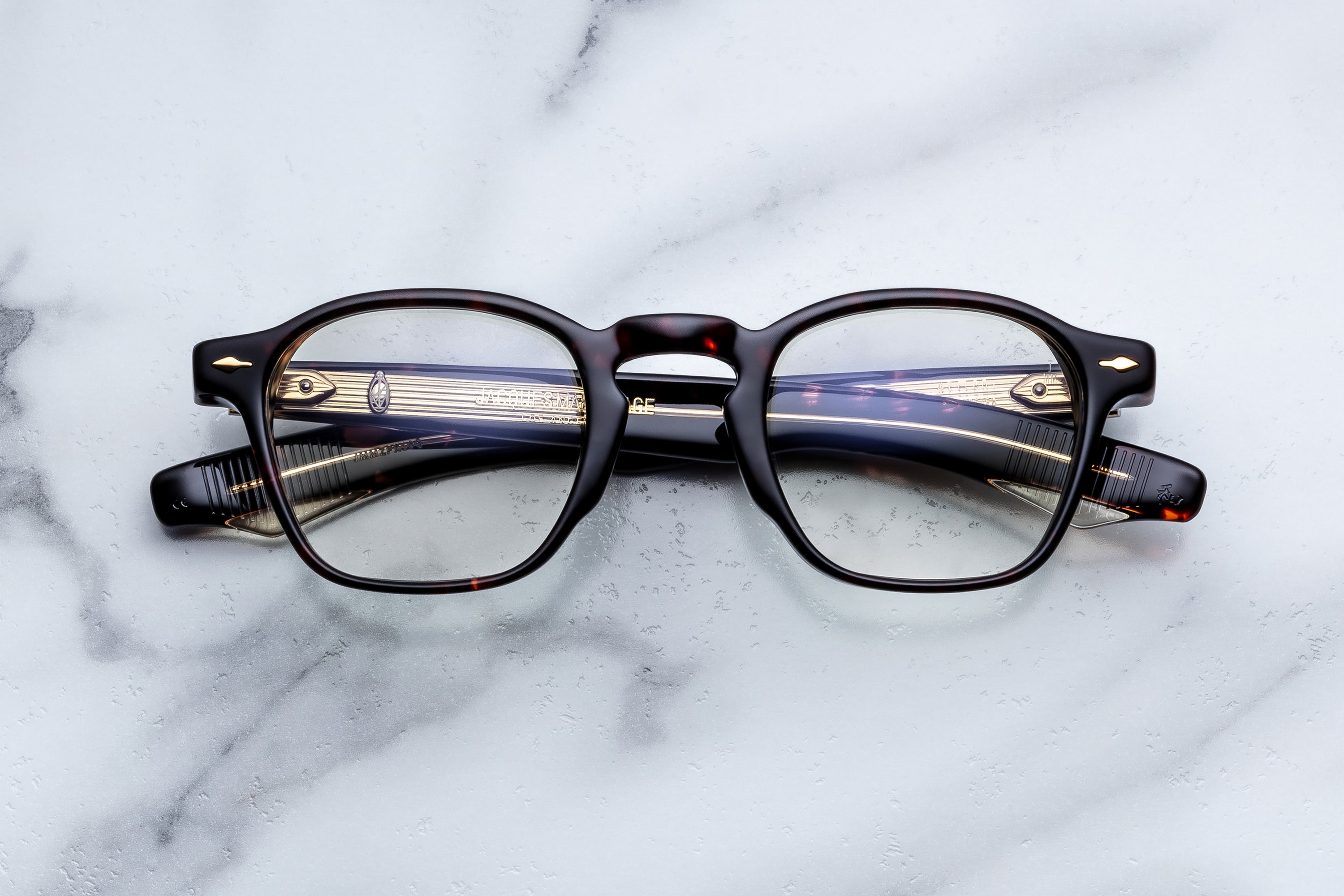 A pair of round-frame eyeglasses with a glossy black front and tortoiseshell temples, resting on a white marble surface.