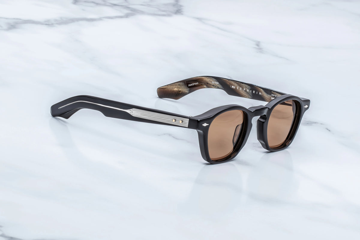 Jacques Marie Mage Zephirin sunglasses with brown lenses and sculpted temple construction resting on a white marble surface.