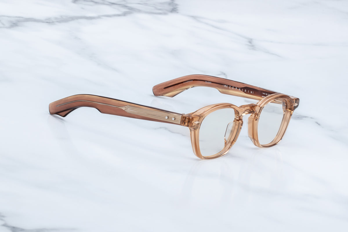 Translucent tan Jacques Marie Mage Zephirin spectacles with gold-tone sculpted temple detailing on a white marble surface.