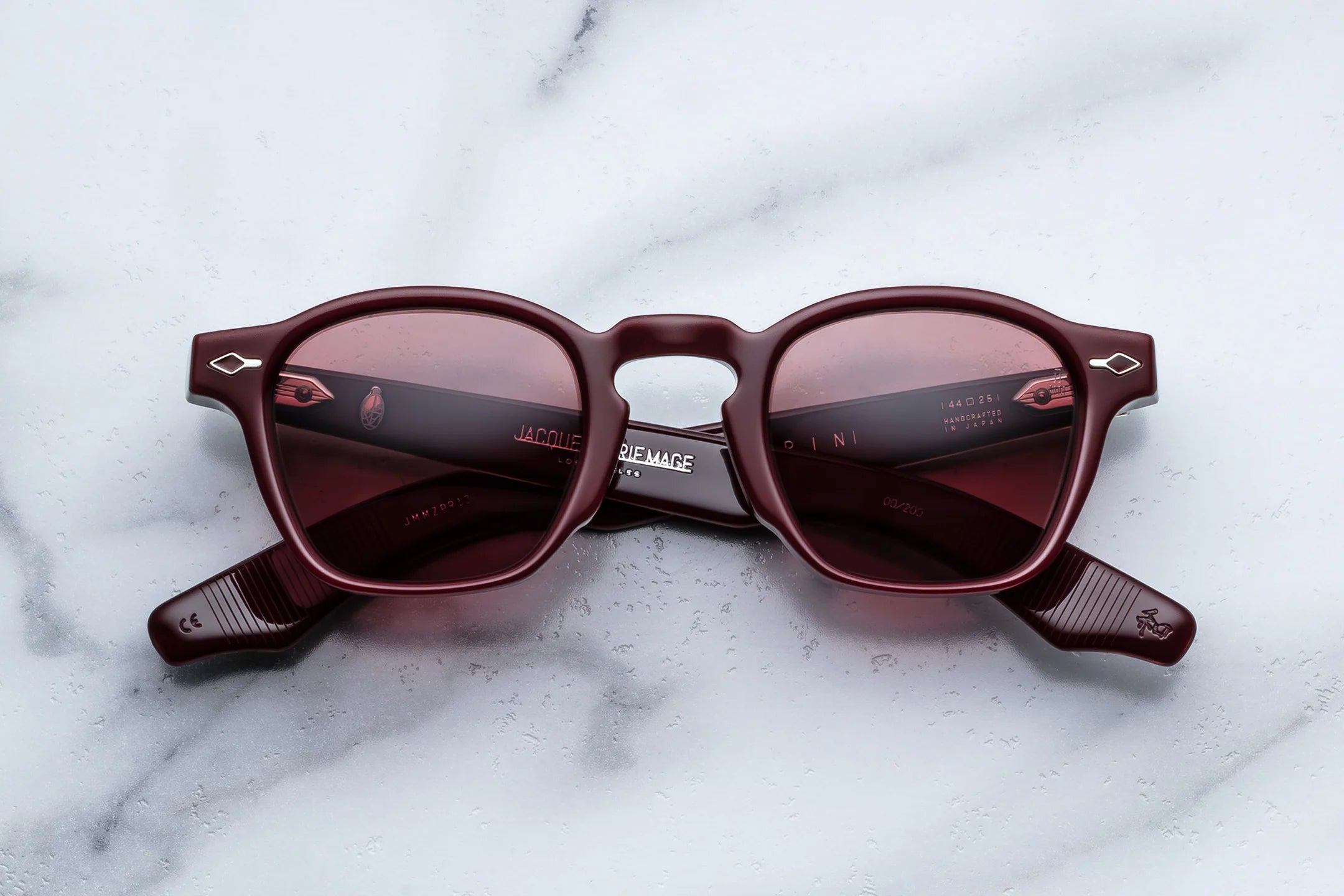 JMM Maroon sunglasses with gold accents on a marble surface