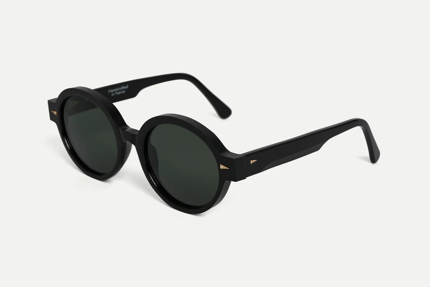 Round black sunglasses with dark lenses and small gold geometric accents on the temples, shown on a light gray background.