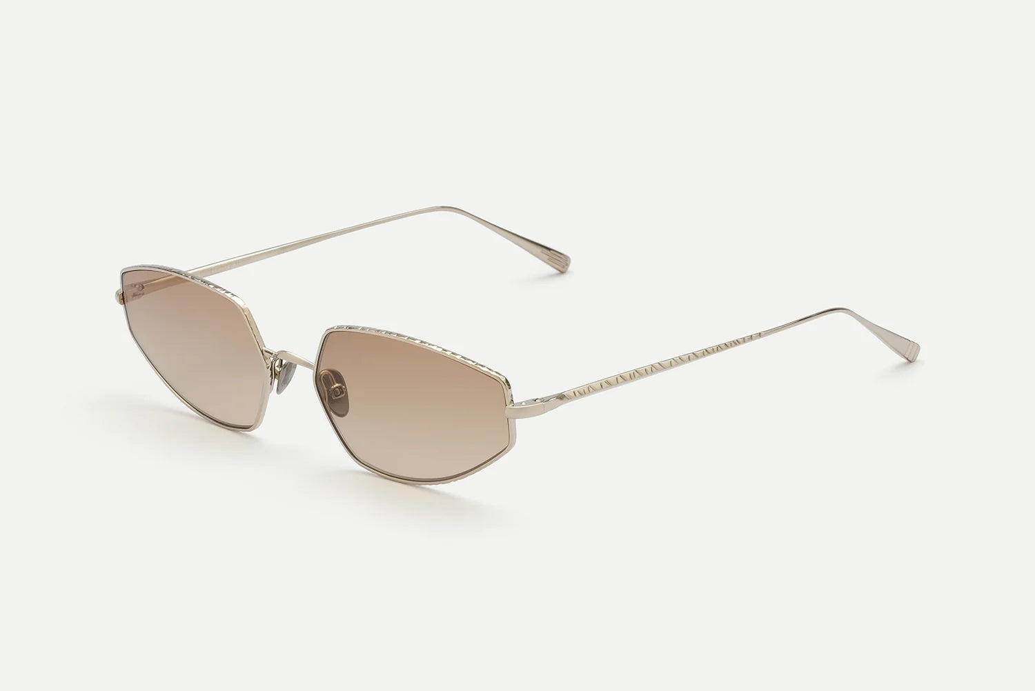 The AHLEM Yvonne by AHLEM features gold metal sunglasses with thin frames, angular brown-tinted lenses, and slim arms—displayed on a white background at a three-quarter angle—that showcase a subtle Bauhaus design influence and are meticulously handcrafted in France.