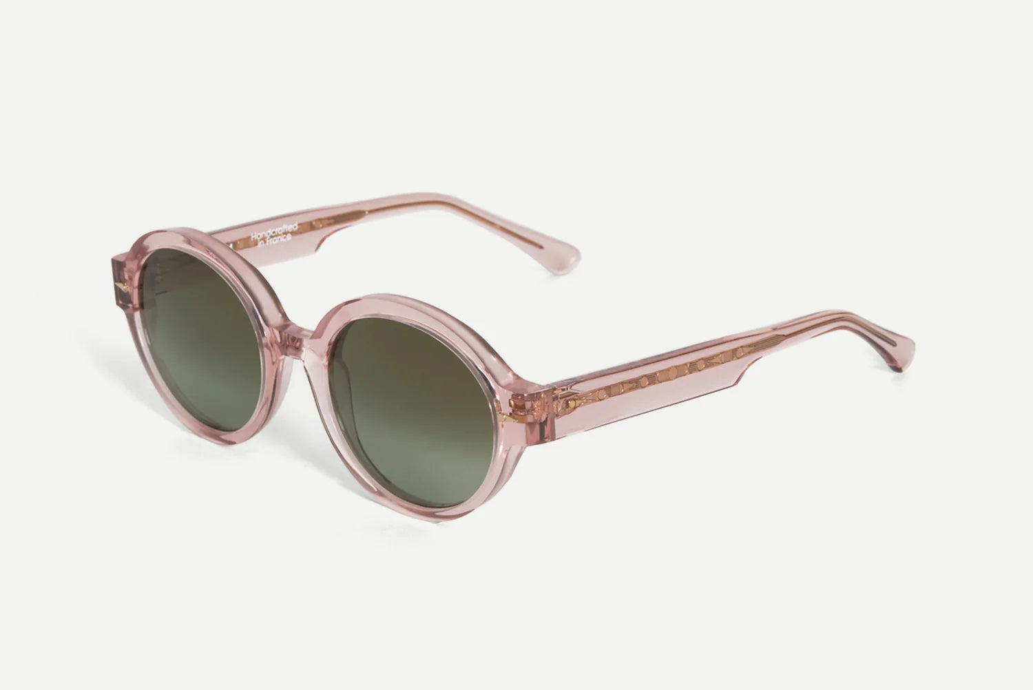 Oversized round sunglasses with translucent dusty pink frames and dark green lenses, shown on a light gray background.