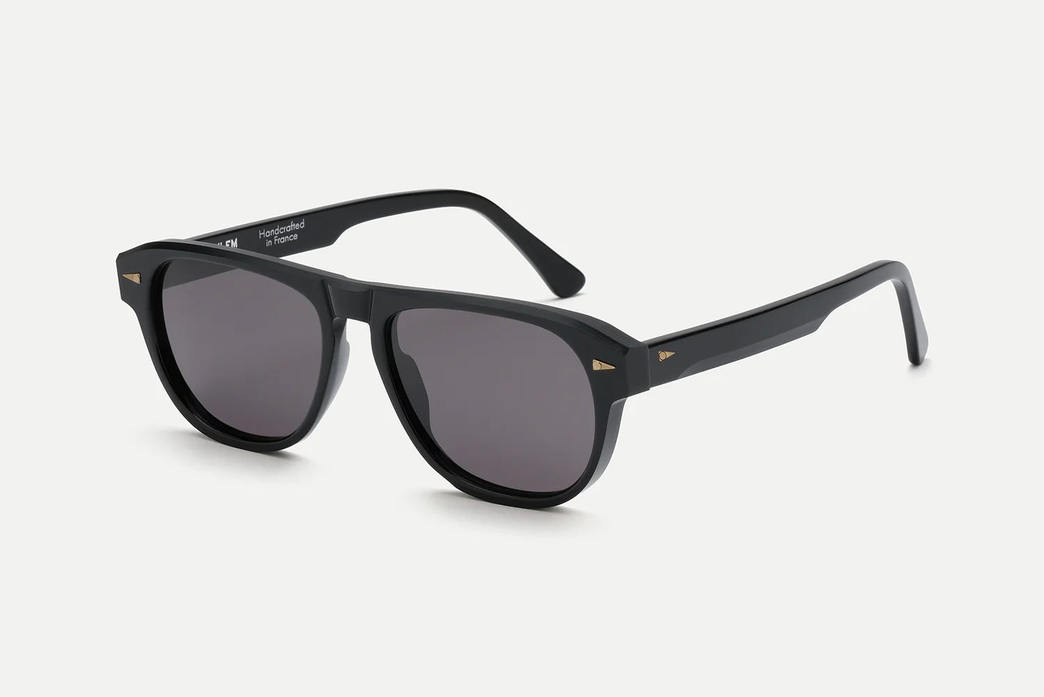 AHLEM Carpentier sunglasses by AHLEM are shown on a white background. The frame, handcrafted in France from premium Italian acetate, is thick and glossy with a slight curve at the temples and small gold accents near the hinges. The black design features dark lenses for a classic look.