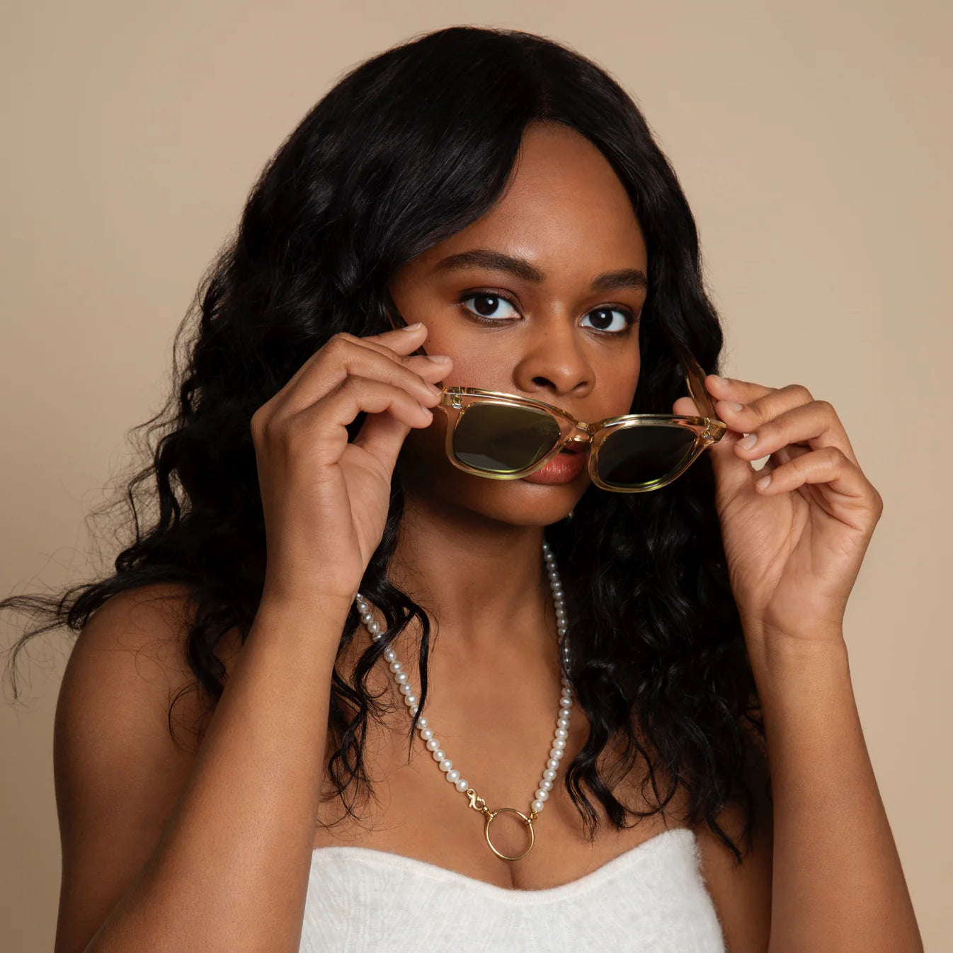 Woman holding sunglasses up to her face against a beige background